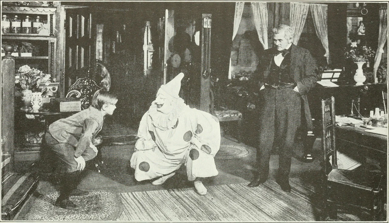 A child actor leans toward a seated clown while an older actor watches on a domestic stage set